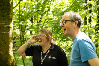 A member of Cumbria Wildlife Trust staff and a member of the public laughing together in a woodland