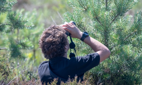 image of young conservationist, Andy Macaulay using binoculars out in the field