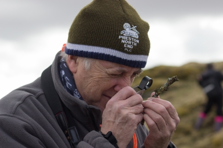 Man in hat using hand lens to study lichen on twig