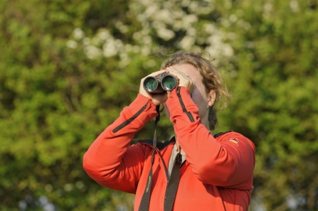 A woman in red top looking through binoculars outside in nature - copyright Terry Whittaker 2020VISION