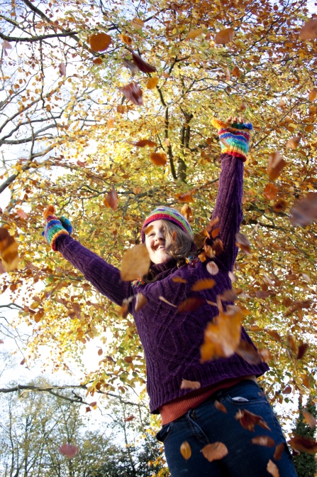 Woman playing in autumn leaves in cozy jumper - copyright Tom Marshall