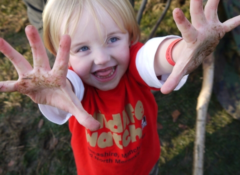 child with muddy hands wearing a Wildlife Trust Wildife Watch tee shirt