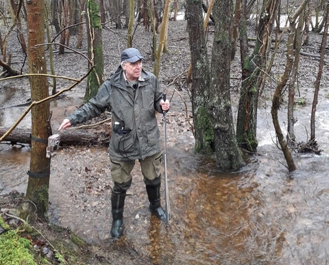 A man in wellies and outdoor gear standing in shallow water