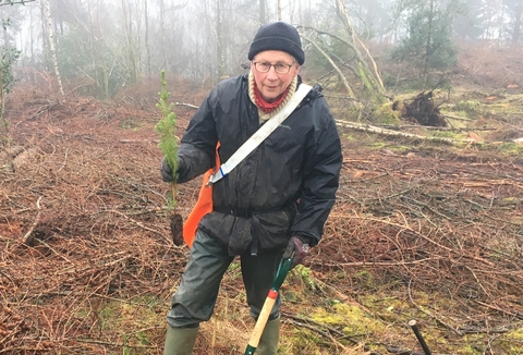 A man holding a small plant and a spade