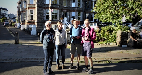 A group of four people standing on a town street, some holding binoculars.