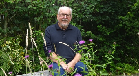 A smiling, grey-haired man sitting in his garden in summer