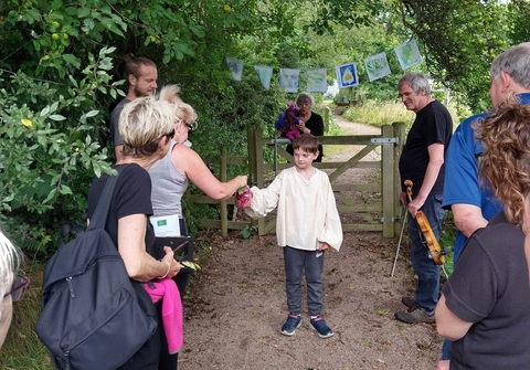 A young boy dressed in costume acting in a play in the outdoors, with an audience standing around.