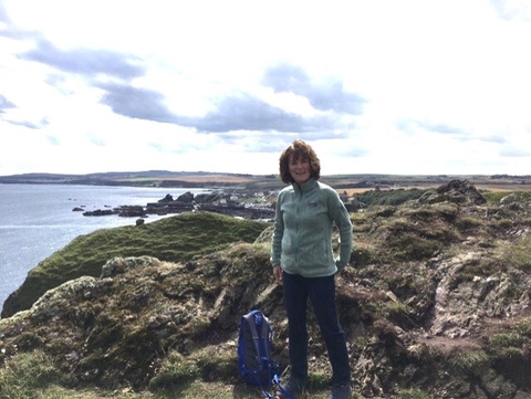 A woman in a fleece standing next to a rucksack on a rocky cliff at the coast.