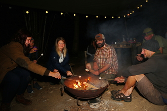 A group of people sitting around a campfire, toasting marshmallows