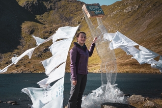 Amy Bray standing next to her Another Way sculpture in the mountains, with a lake behind her.