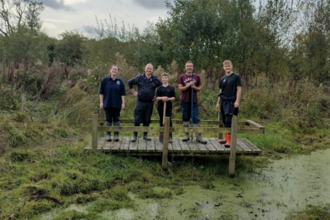 A group of five people standing on a wooden platform over a pond. 