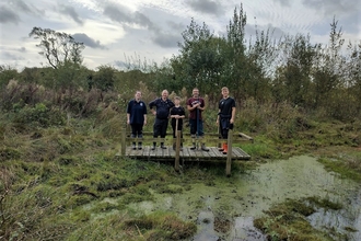 A group of five people standing on a wooden platform over a pond. 
