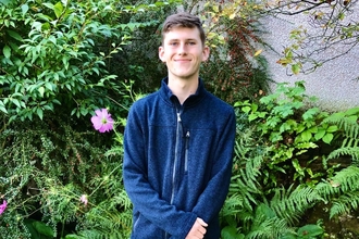 A young man in a fleece standing in front of garden greenery