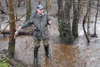 A man in wellies and outdoor gear standing in shallow water