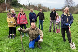 A group of people of various ages standing in a field, holding gardening tools