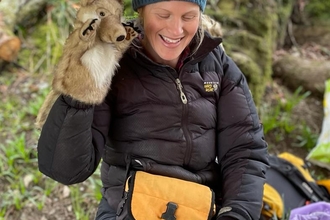 A woman sitting in a forest with a wolf hand puppet on her hand