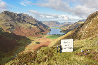 Two people placing a canvas that says 'each act matters' on a fell above a lake. 