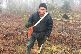 A man holding a small plant and a spade 