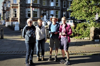 A group of four people standing on a town street, some holding binoculars.