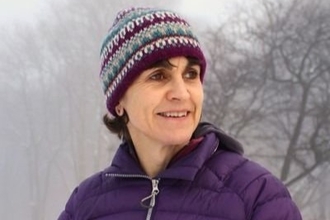 A woman in a woolly hat and insulated jacket smiling and looking to the right away from the camera