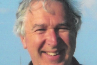 A portrait shot of a smiling man with grey hair