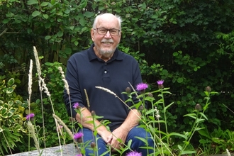 A smiling, grey-haired man sitting in his garden in summer