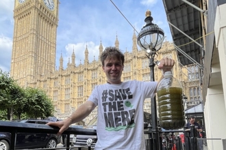 A man in a #SaveTheMere t-shirt, holding up a big bottle of grim-looking green water