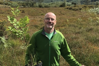 A man in a field holding a tree he's about to plant