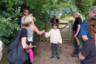 A young boy dressed in costume acting in a play in the outdoors, with an audience standing around.