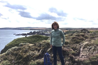 A woman in a fleece standing next to a rucksack on a rocky cliff at the coast. 