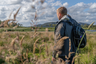 A man stands in a nature reserve surrounded by long grasses on a sunny day