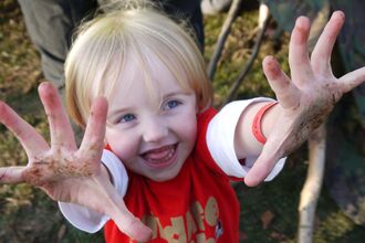 child with muddy hands wearing a Wildlife Trust Wildife Watch tee shirt