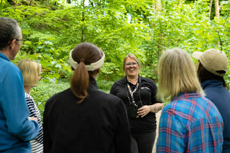 A group of people standing around a smiling group leader, against a woodland backdrop