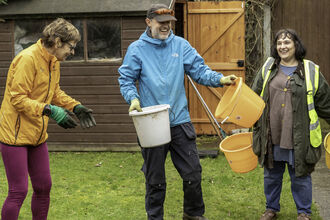 Three people outdoors in a garden holding buckets © Penny Dixie