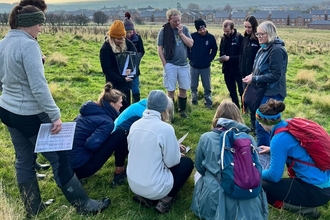 A community group gathered outdoors on grassland with Cumbria Wildlife Trust outside a town