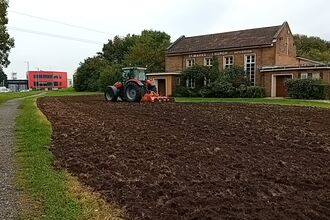 A tractor ploughs a grass area in front of a church.