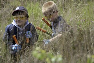 two chidren outdoors wearing protective goggles and gloves and holding gardneing sheers