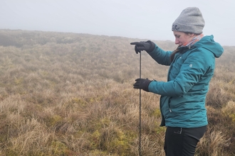 Person standing on a remote peatland in the cloud, monitoring the hydrology