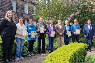 Group of volunteers holding certificates for Badger's Paw Award in garden of Tullie 