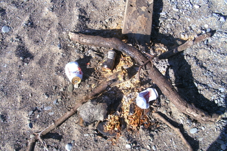 Remnants of a campfire on the beach, including cans & bottles
