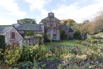Photo shows the garden at Acorn Bank, with the house in the background and flower beds in the foreground