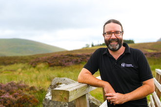 Pete Jones Cumbria Wildlife Trust standing leaning on a gate with Skiddaw in the background