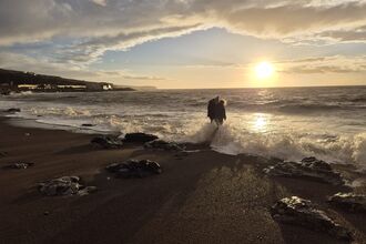 The silhouettes of two children splashing in the waves as the sun goes down. 