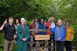Group of people surround wooden sign for new Victoria Wood Nursery, Plumgarths