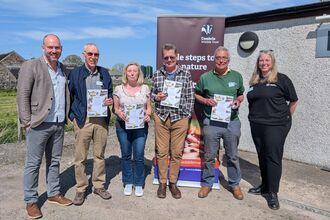 Group of men and women hold up Badger's Paw award certificates in front of Cumbria Wildlife Trust banner