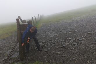 A man dressed in waterproofs mending a fence on top of a misty gravel path