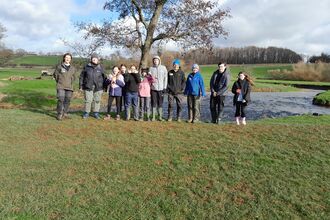 A group of young people and leaders on a river bank in front of a tree.