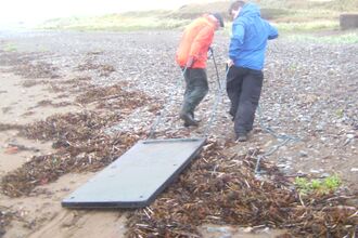 Large slab of solid plastic being towed from the beach by volunteers