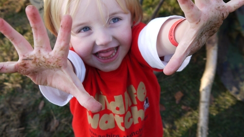 child with muddy hands wearing a Wildlife Trust Wildife Watch tee shirt