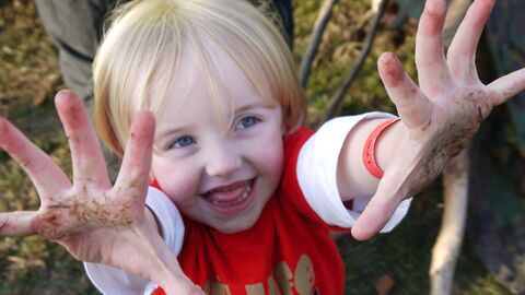 child with muddy hands wearing a Wildlife Trust Wildife Watch tee shirt